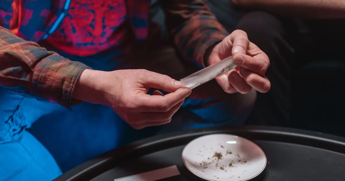 Hands rolling a thin, see-through rolling paper over a dark table